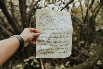 Hand holding handwritten poetry note in British Columbia forest.