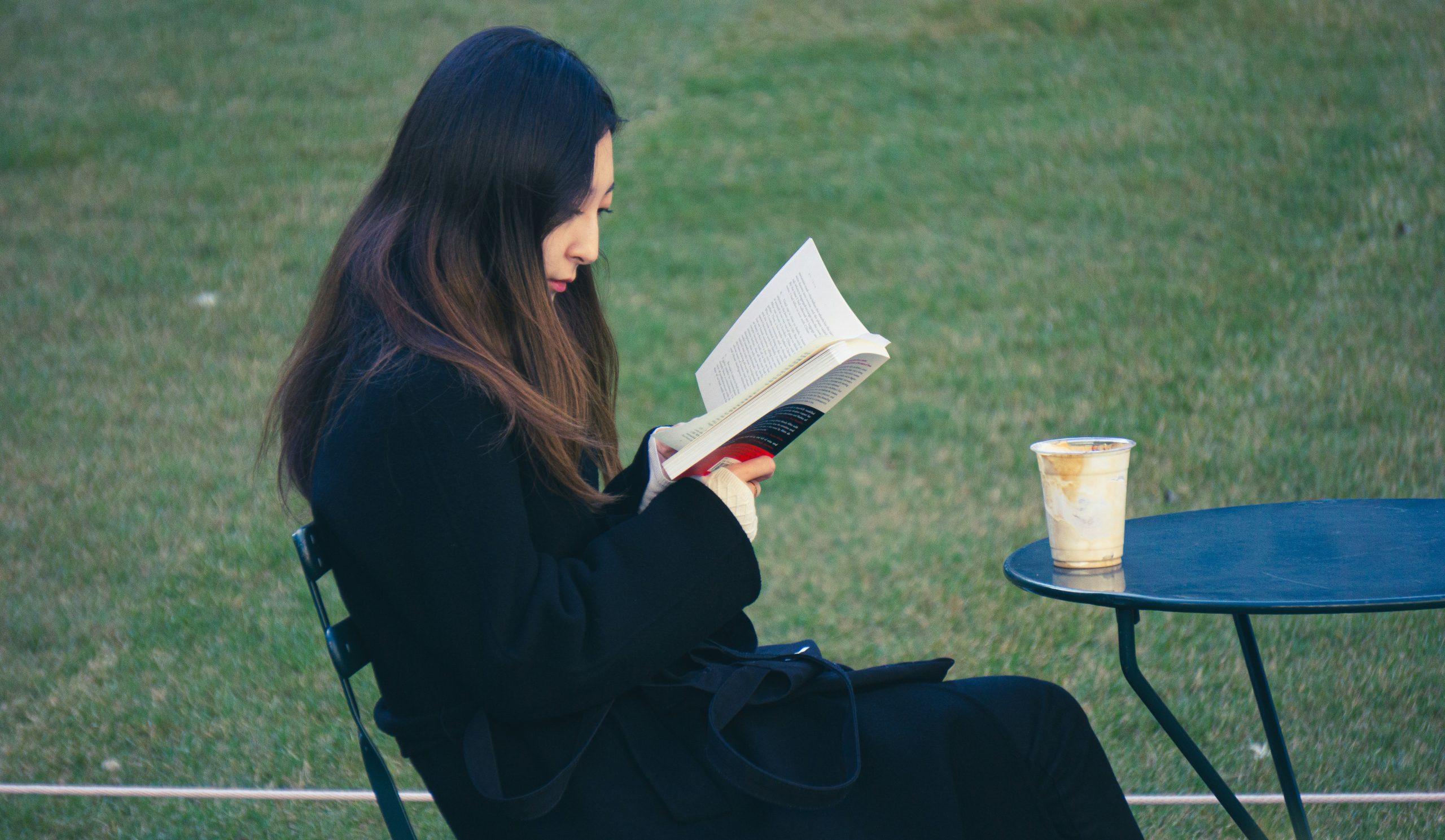 Woman reading a book outdoors with coffee on a sunny day.